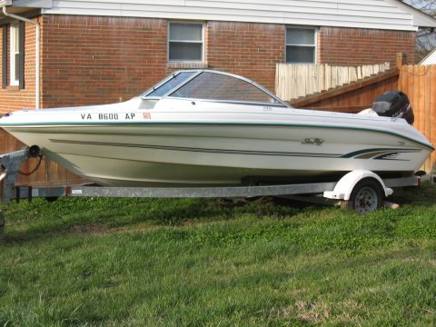 1994 Ford Bronco - A white Sea Ray boat is parked on a trailer in front of a brick house and wooden fence.