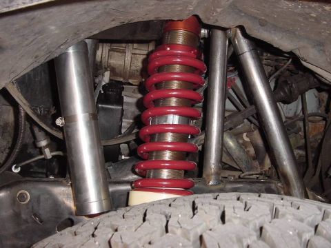 1987 Ford Bronco - Close-up view of a vehicle's coilover suspension system, showing red springs and silver components.
