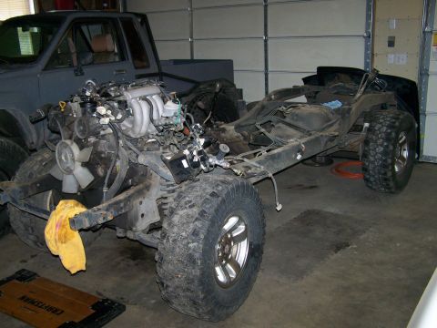 1988 Suzuki Samurai - A 1988 Suzuki Samurai chassis is shown with its engine and front suspension, with another vehicle partially visible in the background.