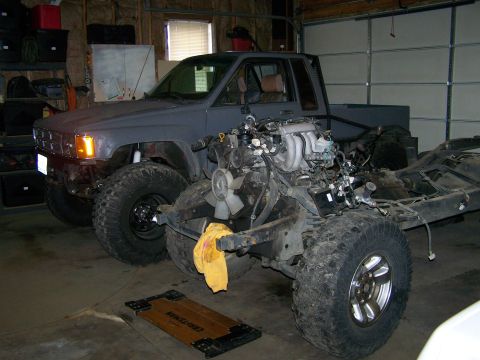 1988 Suzuki Samurai - A pickup truck's chassis is visible with its engine removed, parked next to another truck in a garage.
