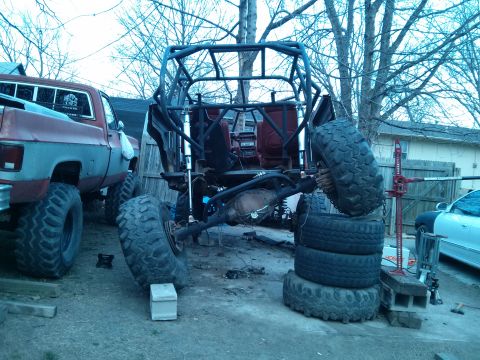 1986 Ford Bronco - Custom off-road buggy chassis with oversized tires is seen next to a pickup truck in a yard.