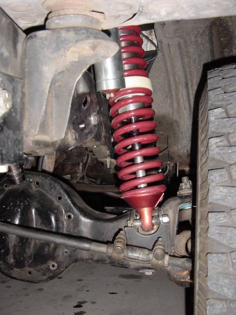 1987 Ford Bronco - Vehicle suspension system detail showing a red coilover shock and axle components.