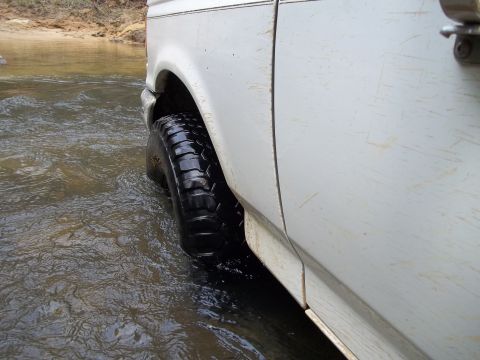 1990 Ford Bronco - A white SUV navigates through a shallow body of water, with its front tire submerged.