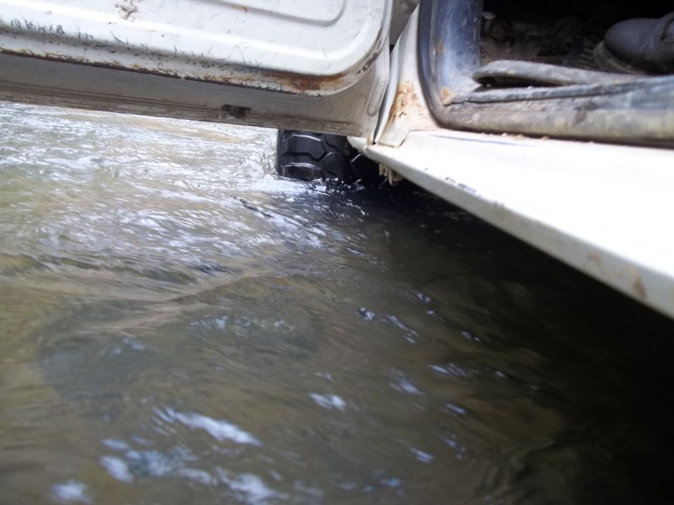 White vehicle door open, tire in water, rust on door frame