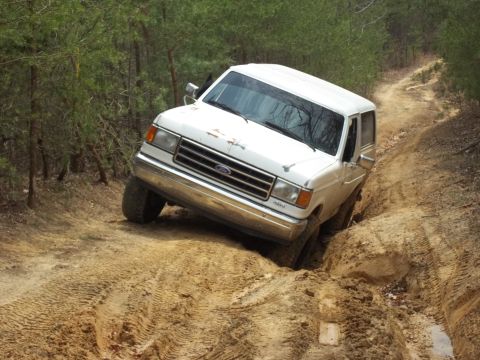 1990 Ford Bronco - White 1990 Ford Bronco tackling a challenging dirt path in a wooded area.