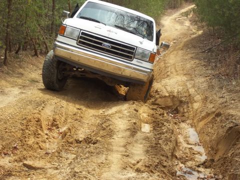 1990 Ford Bronco - A white Ford Bronco navigates a muddy, off-road trail.
