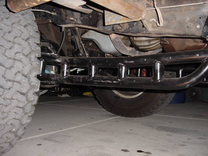 Underside of vehicle showing welded tubular crossmember and off-road tires on garage floor
