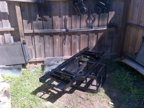 1994 Ford Bronco - A disassembled vehicle frame and radiator are stored outdoors near a wooden fence, suggesting a repair or restoration project.