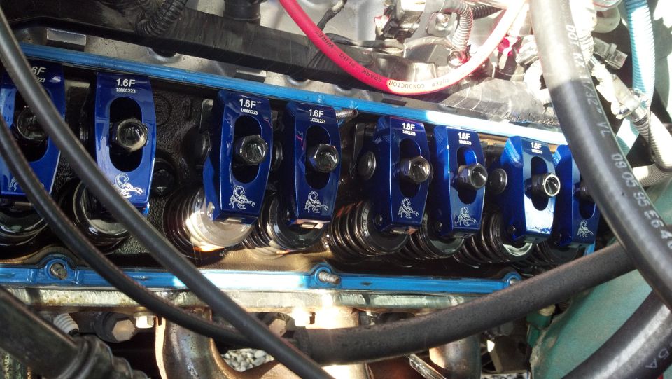 Close-up of blue aftermarket rocker arms with '1.6F' and a scorpion logo, installed on an engine