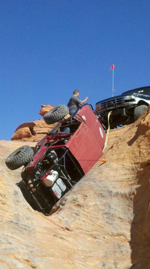 1994 Ford Bronco - Two off-road vehicles are stuck on a steep, rocky incline under a clear blue sky.