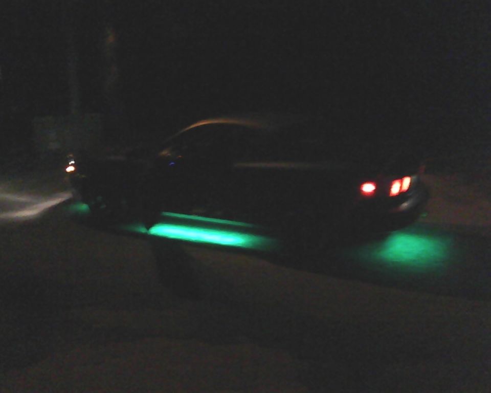 Car with green underglow lights at night, rear view visible