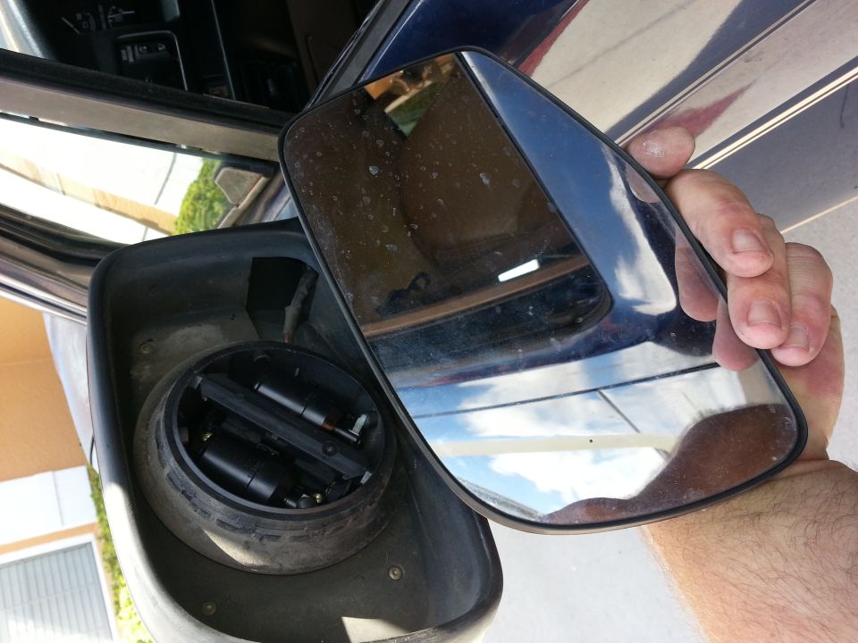 Side mirror assembly removed from a dark blue vehicle, showing internal components and a reflection of the interior