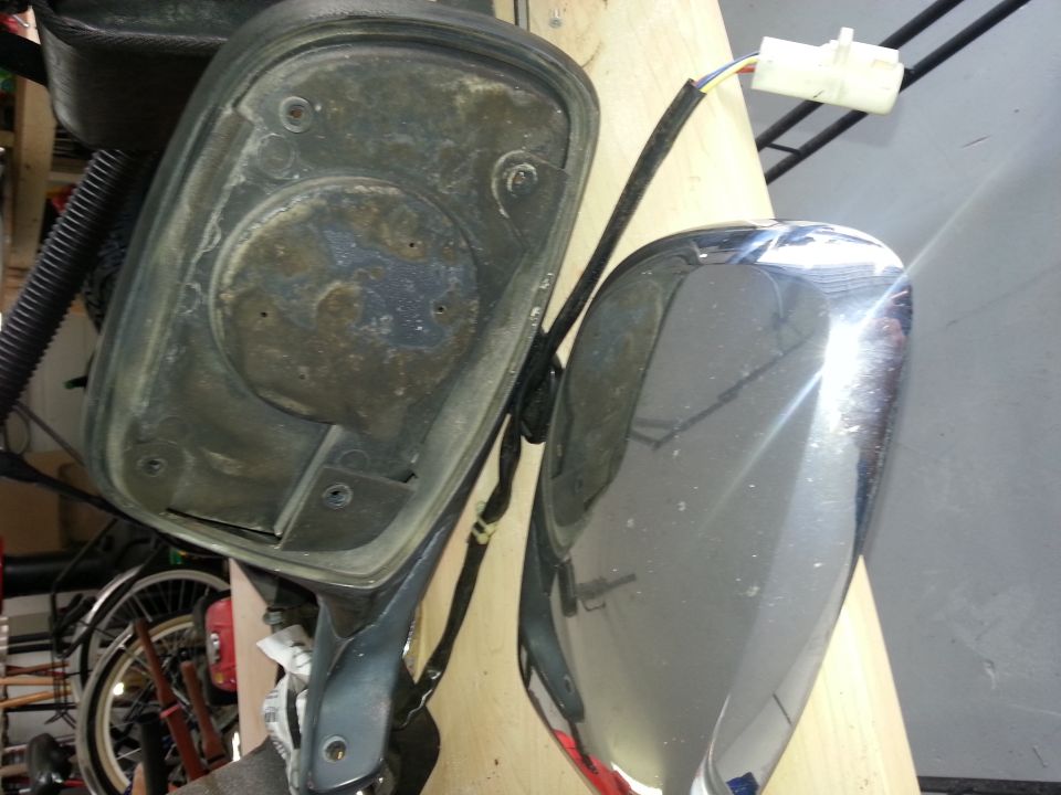 Disassembled car side mirror assembly, showing the backing and the chrome-finished mirror housing