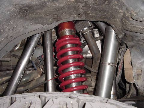 1987 Ford Bronco - Close-up view of a red coilover suspension system, likely from an off-road vehicle, with visible metal tubing and a tire tread.