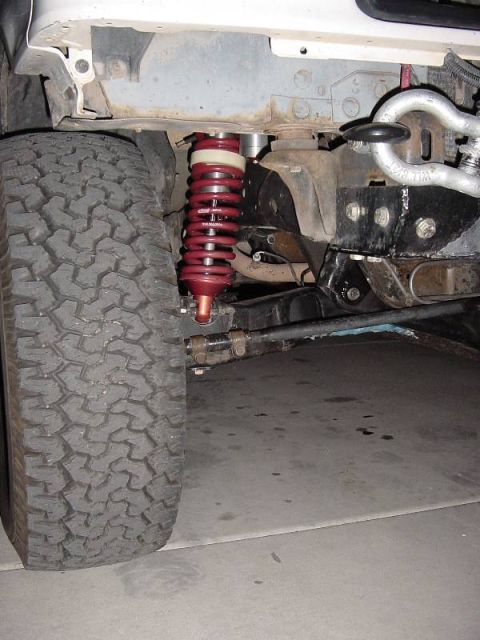 1987 Ford Bronco - Close-up view of a red coilover suspension system and a large tire, likely part of an off-road vehicle's suspension.