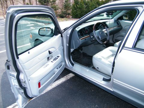 2004 Ford Crown Victoria - Interior view of a 2004 Ford Crown Victoria, showing the dashboard, steering wheel, and front seats with the driver's door ajar.