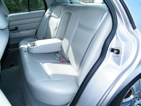 2004 Ford Crown Victoria - The back seat area of a car features light gray leather upholstery and a fold-down armrest with cup holders.