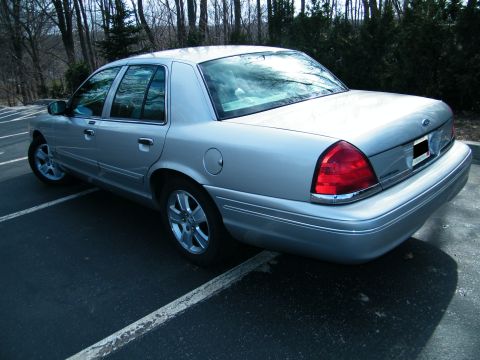2004 Ford Crown Victoria - Silver sedan with chrome accents and aftermarket wheels is viewed from the rear three-quarter angle in a parking lot.