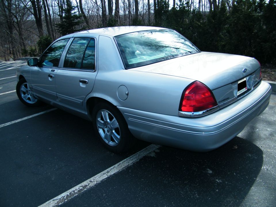 Silver sedan parked in a lot, rear three-quarter view. Chrome trim along the lower body and around taillights. Aftermarket wheels