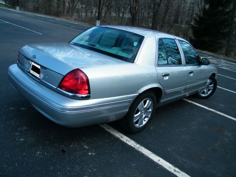 2004 Ford Crown Victoria - Rear view of a silver 2004 Ford Crown Victoria parked in a lot with trees in the background.