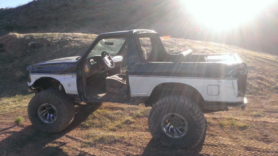 Lifted black and white Bronco with doors removed, parked outdoors