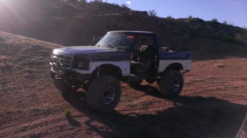 1994 Ford Bronco - Modified 1994 Ford Bronco sits on a dirt hill with its driver's door ajar.