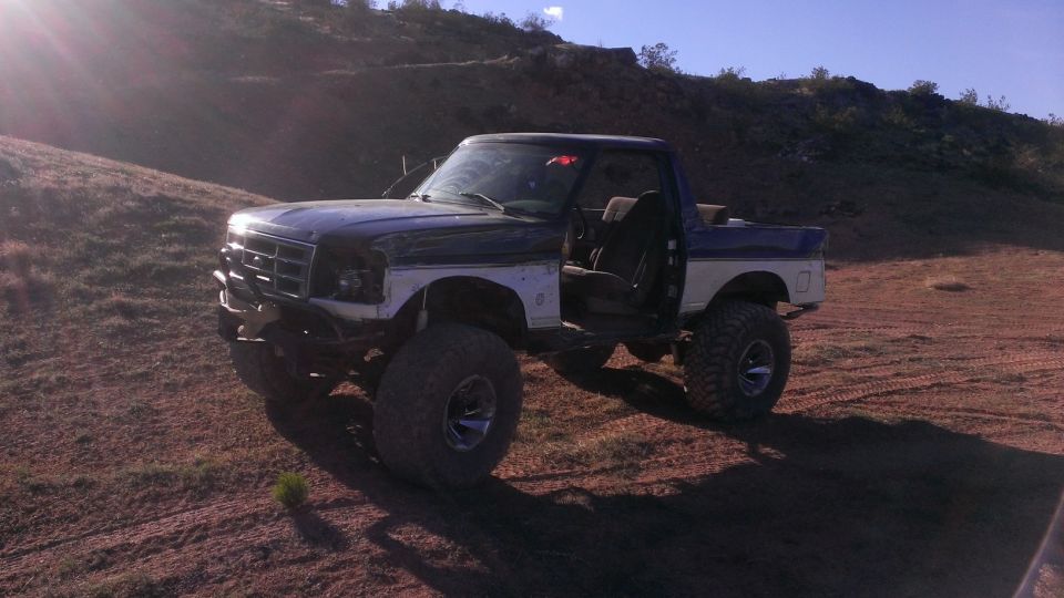 1994 Ford Bronco with lifted suspension and off-road tires, driver's door open, parked on dirt terrain
