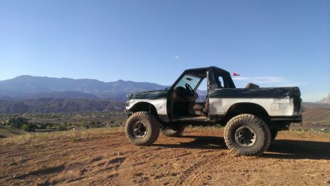 1994 Ford Bronco - A lifted 1994 Ford Bronco sits on a dusty overlook with a vast mountain range behind it.