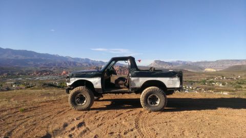 1994 Ford Bronco - Modified Ford Bronco with large tires sits on a dusty hill overlooking a valley and mountains under a clear blue sky.