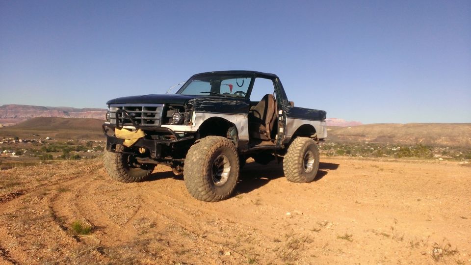 1994 Ford Bronco modified with large tires and off-road bumper, parked on dirt