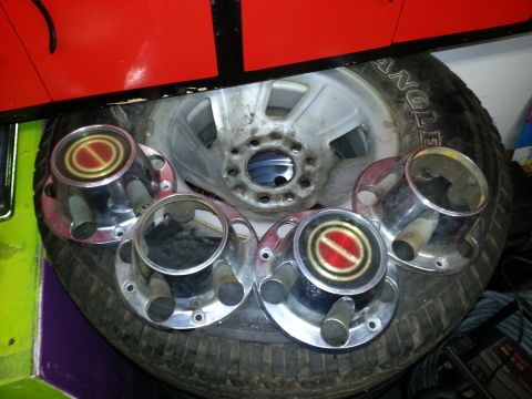 1994 Ford Bronco - Four chrome hubcaps with red and gold centers are displayed on a tire, with a red vehicle panel visible above.