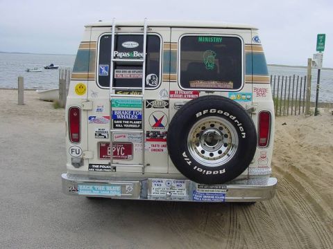 1981 Ford E150 - This van, heavily adorned with bumper stickers, is parked on a sandy area near the ocean.