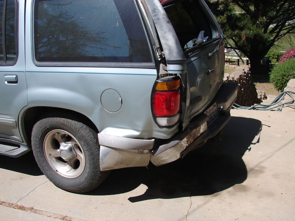 Light blue SUV rear bumper damaged, taillight broken, tire visible