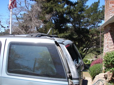 1973 Ford Ranchero - Rear view of a light blue SUV with a roof rack and an open rear door, parked outdoors.