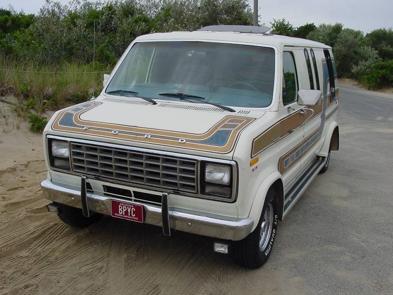 White Ford conversion van, front 3/4 view, on sand with brown stripes and chrome grille