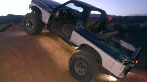 1994 Ford Bronco - Ford Bronco tilted on a dirt hill with doors open at dusk.
