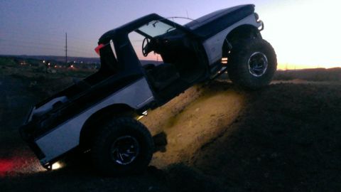 1994 Ford Bronco - A modified Ford Bronco navigates an off-road obstacle during twilight hours.