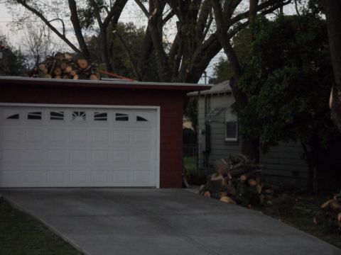 1994 Jeep Cherokee - A suburban scene shows a garage with a white door, a driveway, and piles of cut logs on the roof and beside the house.