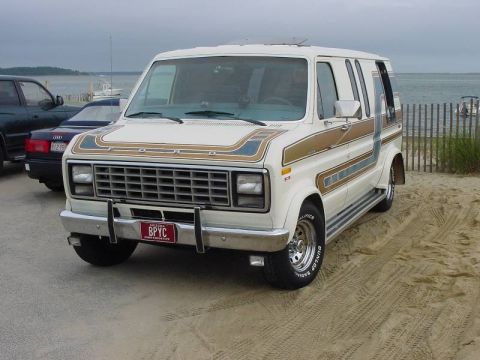 1981 Ford E150 - This 1981 Ford E150 van features distinctive brown and blue racing stripes along its side, seen here parked on a beach.