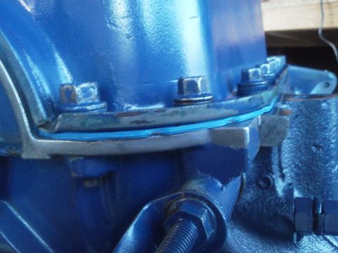 1988 Ford Bronco - A close-up view of a blue engine part, showing a gasket and several bolts securing it in place.