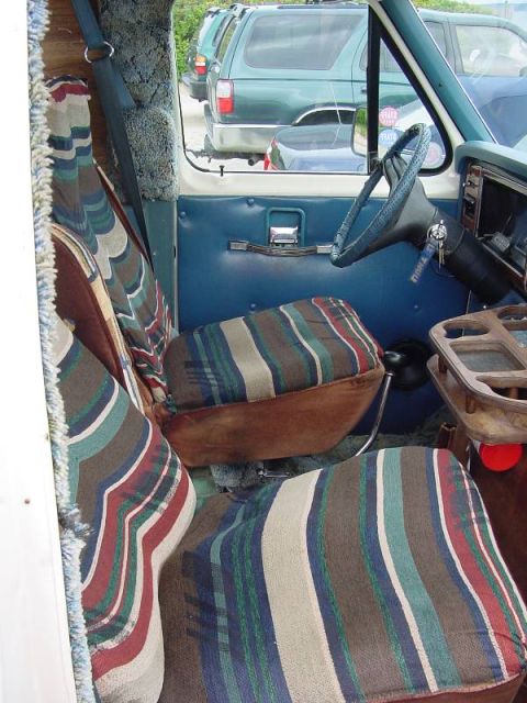 1981 Ford E150 - Interior view of a van showing striped upholstery and a blue door panel. Other vehicles are seen through the window.