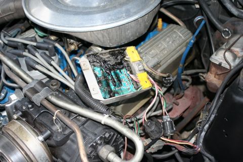 1980 Ford Mustang - A close-up of a damaged electronic control module in a vehicle's engine bay, with visible wiring and engine components.