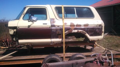 1979 Ford Bronco - A side view of a weathered Ford Bronco body, missing its front end and rear quarter panel, sits on a trailer.