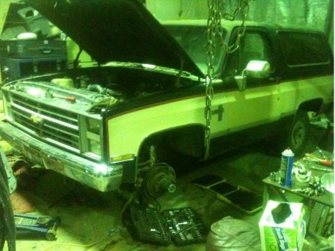 1986 Chevrolet Blazer - A two-tone brown and tan Chevrolet K5 Blazer is shown from the front with its hood open, indicating it is in a repair shop.