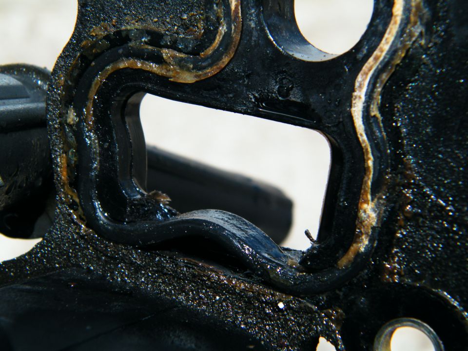 Close-up of a dirty, black engine part with a layered gasket showing signs of wear and oil
