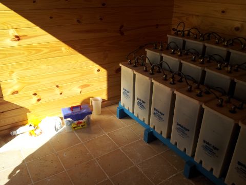 1986 Ford Bronco - A collection of large batteries are arranged on blue racks within a room constructed of wood paneling.
