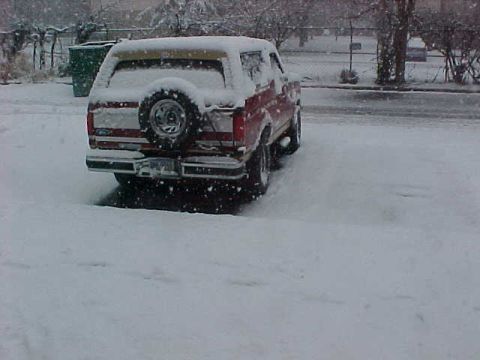 1990 Ford Bronco - A red and yellow Ford Bronco sits covered in snow during a winter storm.