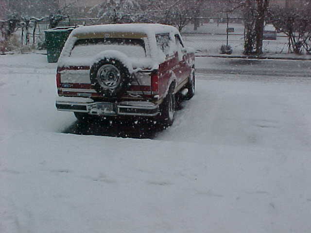 Red and white Ford Bronco rear 3/4 view with snow-covered top and spare tire