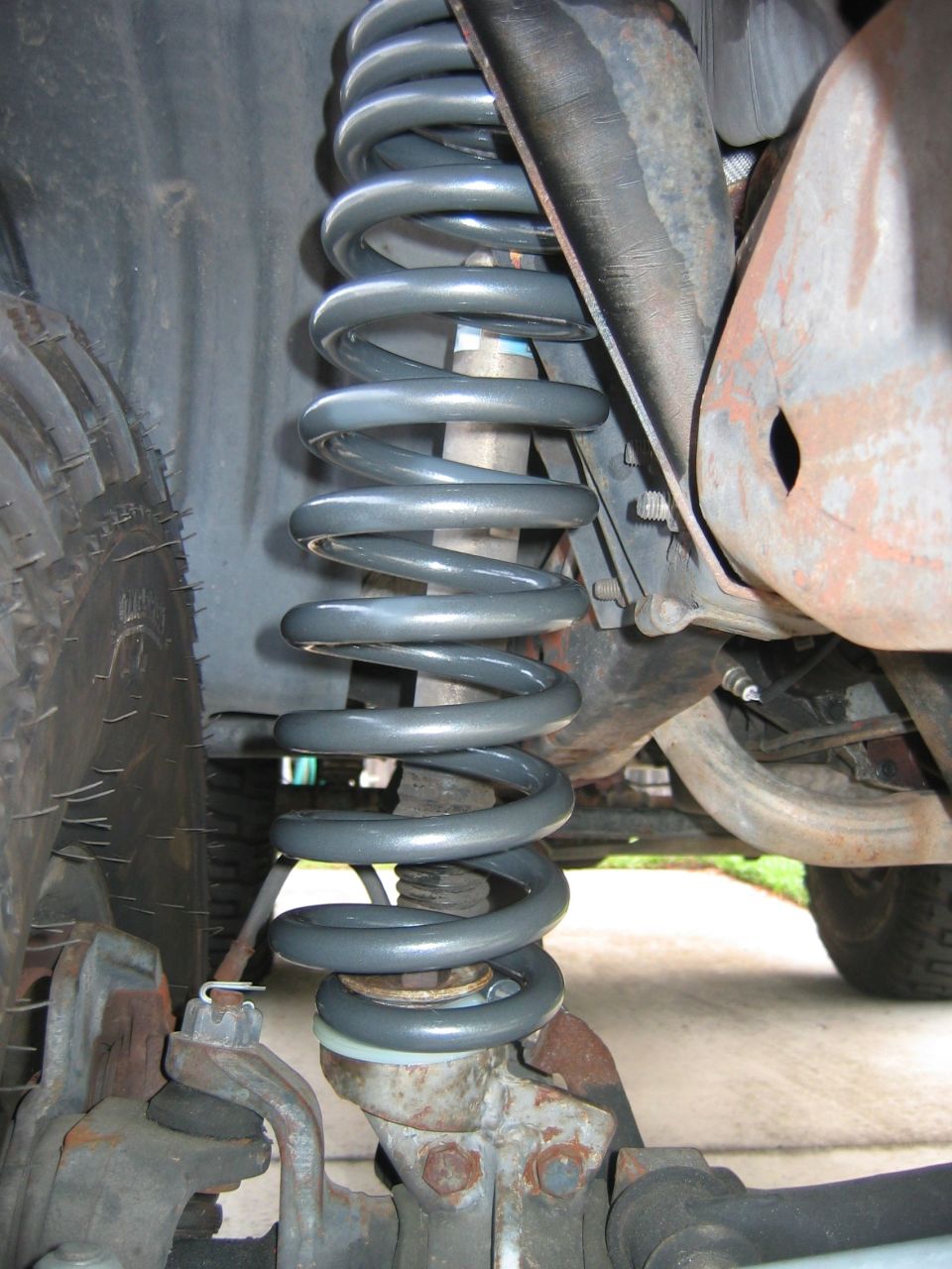 Gray coil spring suspension under a vehicle with rusty frame and tire