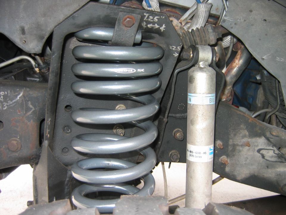 Close-up of a gray coil spring and a silver shock absorber, with some metal brackets and hoses visible